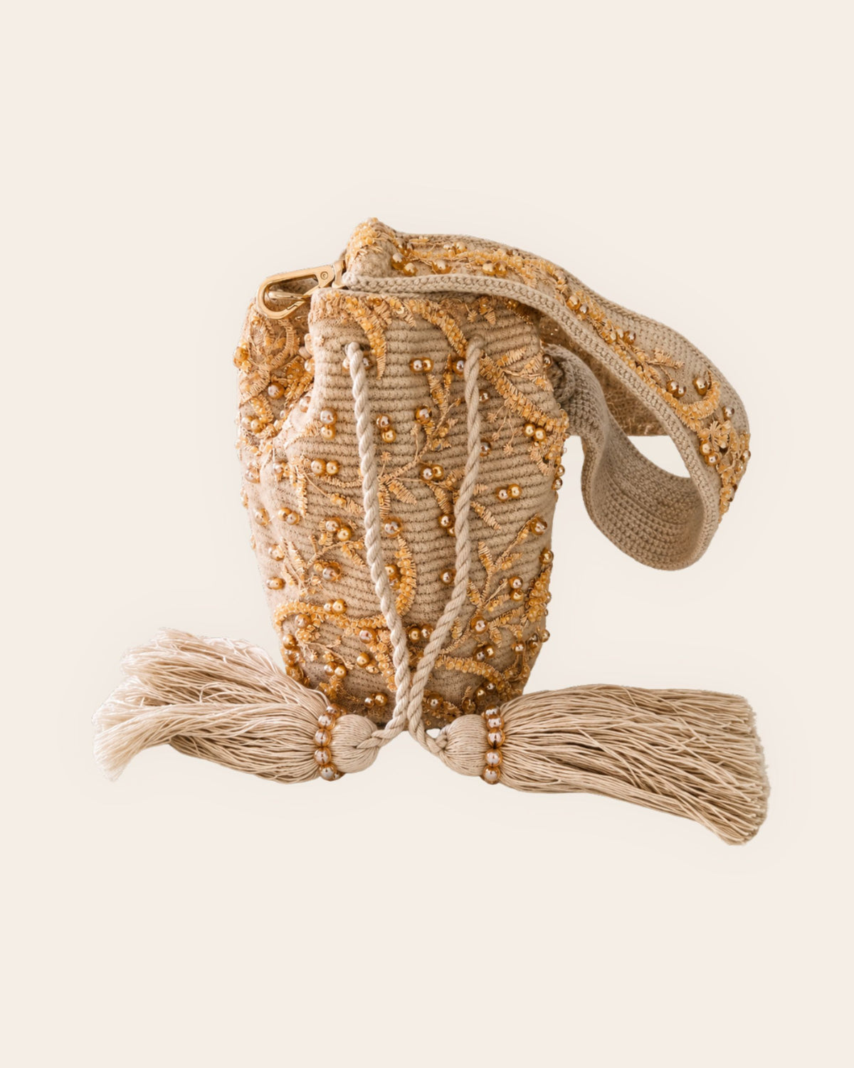 Beige embellished occasion bucket bag with gold beadwork, embroidered botanical details, drawstring tassels and handcrafted handle.