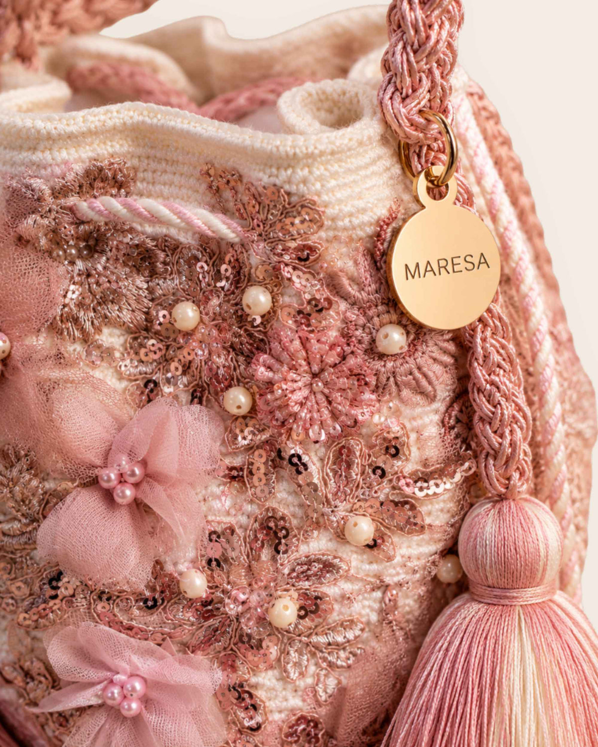 Close-up of pink embellished bucket bag with floral details, tassel and gold-tone Maresa tag