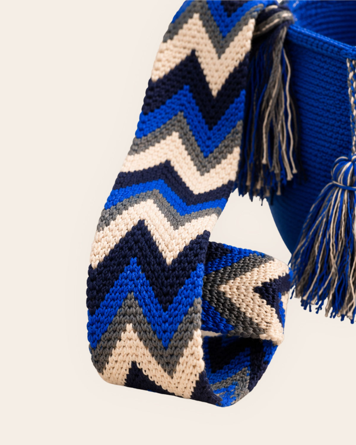 Close-up of woven shoulder strap on cobalt blue Wayuu crochet flap bucket bag with chevron pattern and tassel detail.