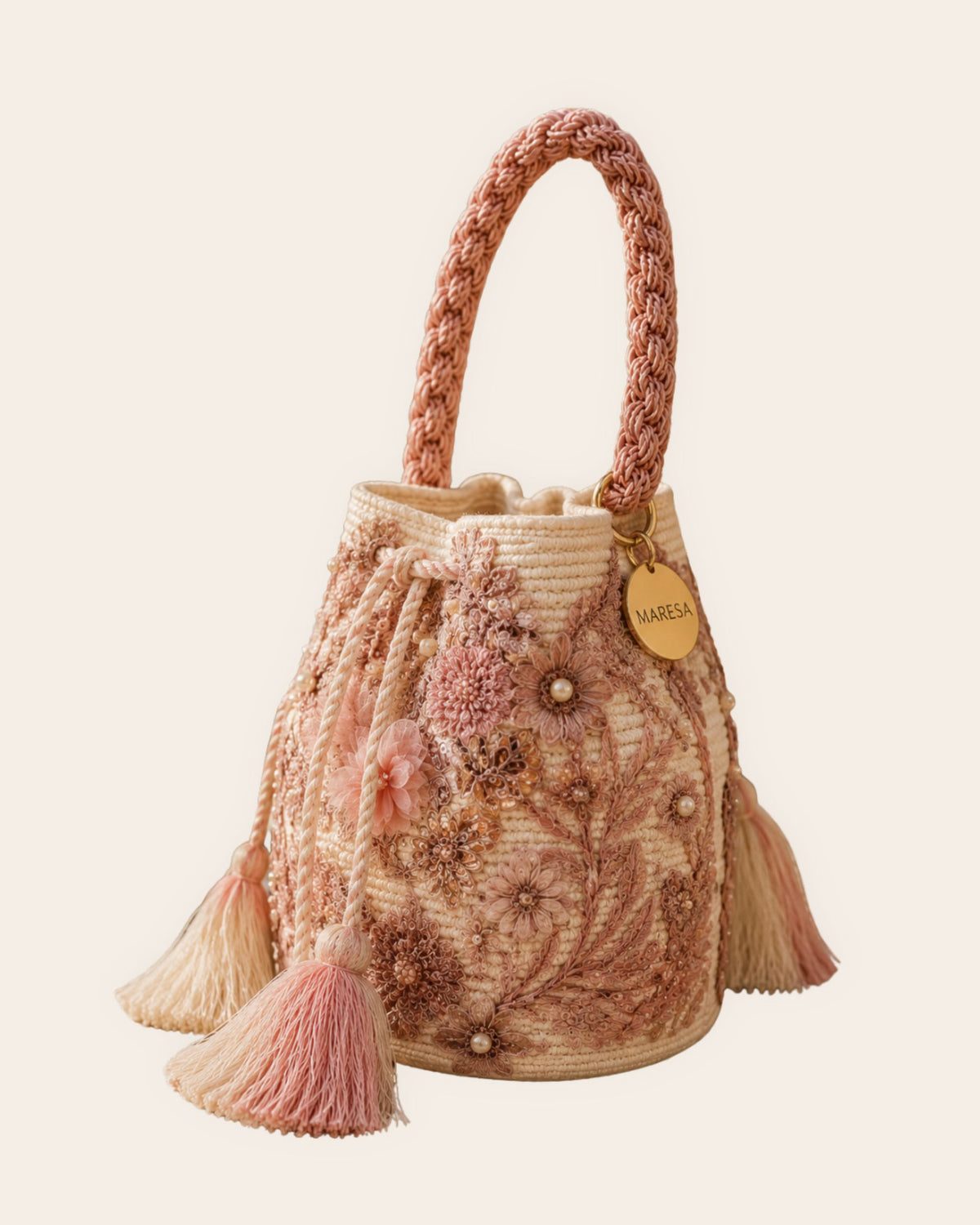 Side view of pink and ivory embellished bucket bag with braided handle, floral details and tassels
