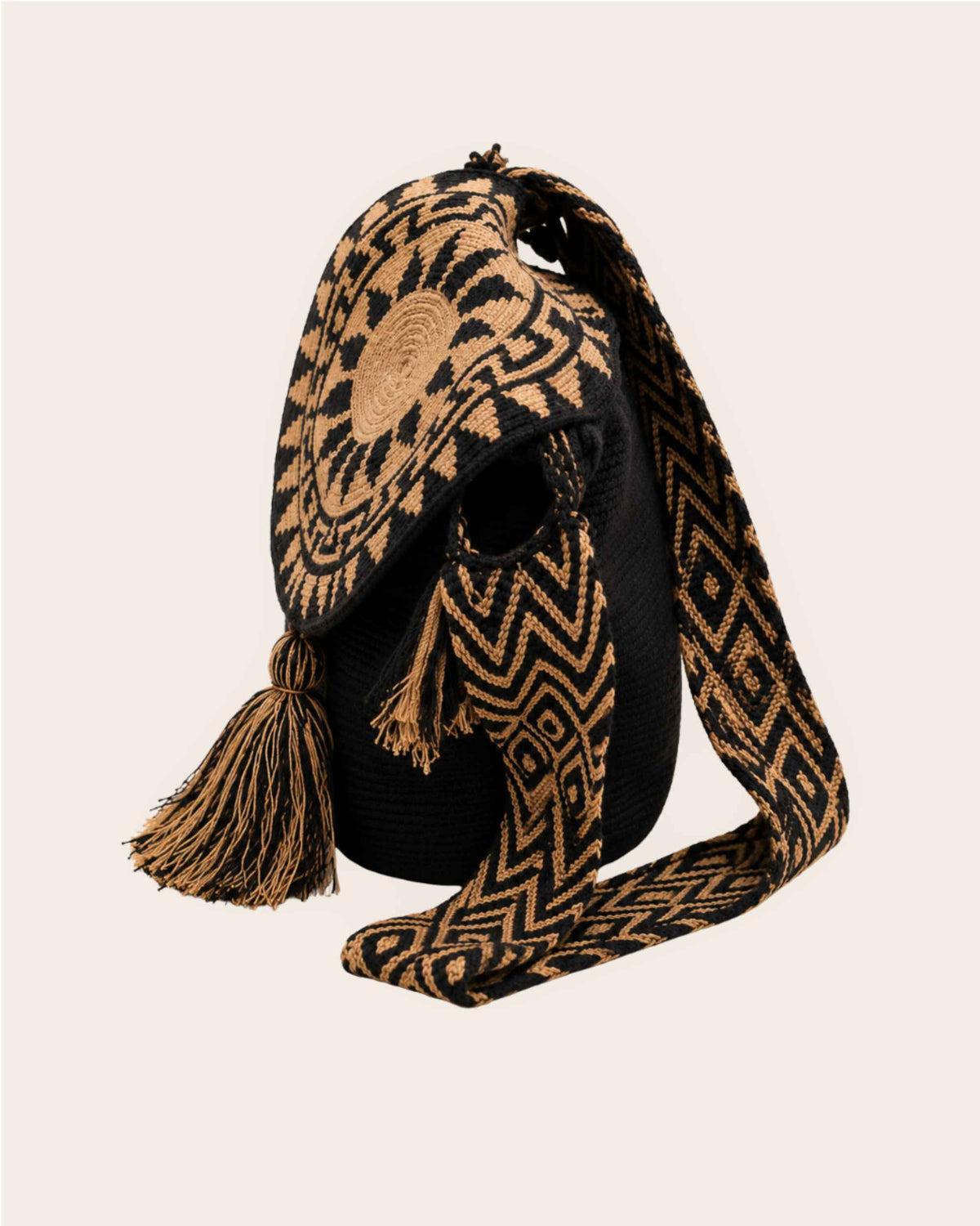 Side view of the black and camel Wayuu crochet Flap Bucket Bag showing the woven strap, circular flap and tassel detail.