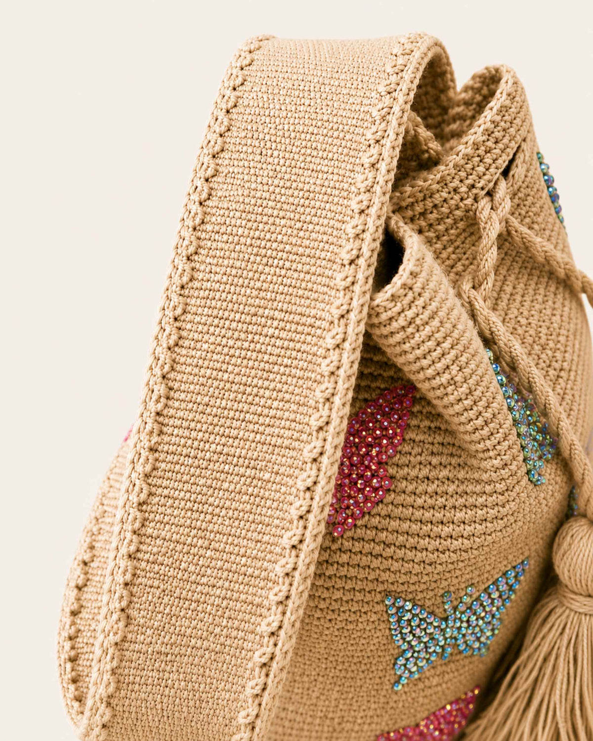 Close-up of wide hand-crocheted shoulder strap and colourful butterfly embellishments on beige Wayuu bag.