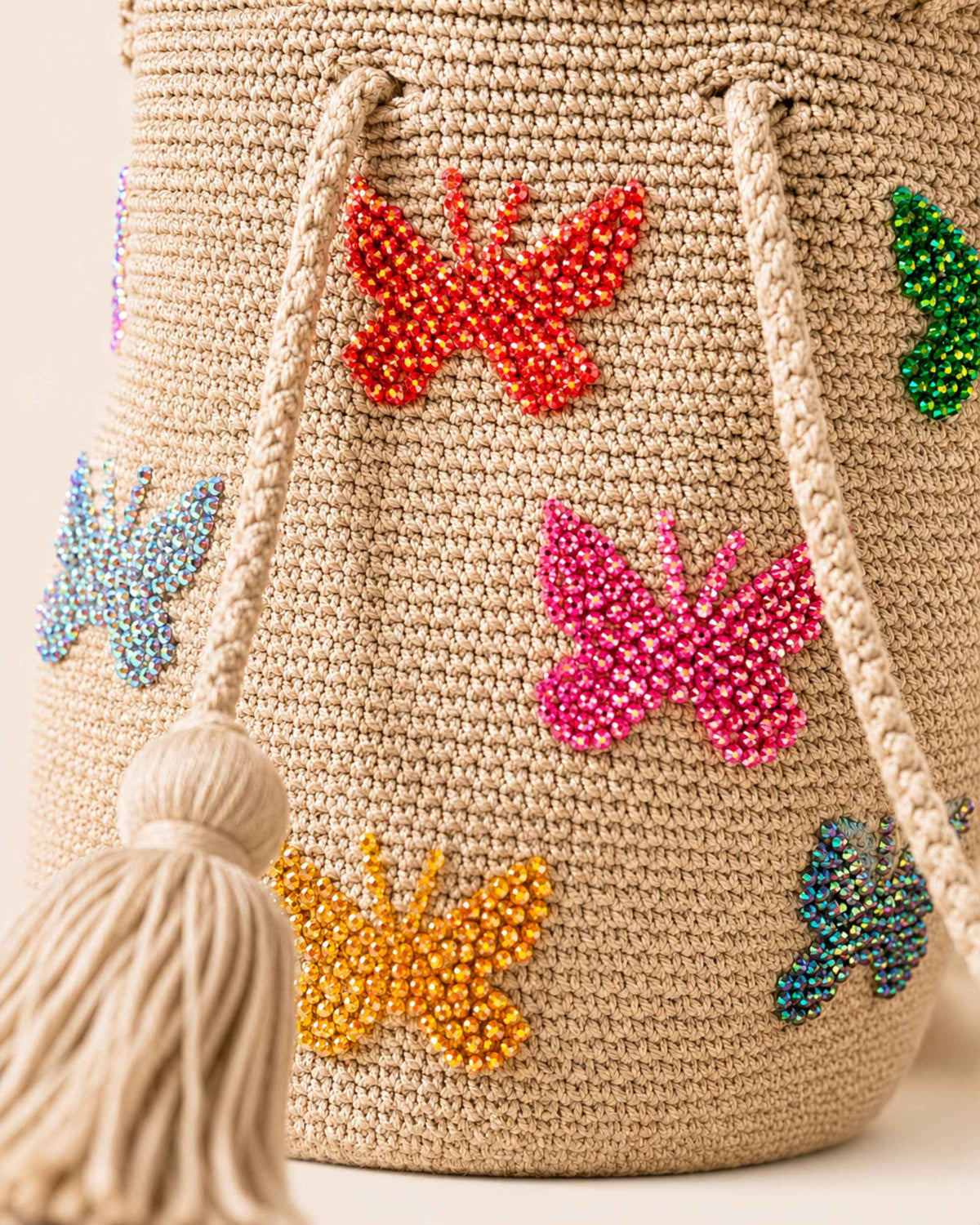 Close-up of colourful hand-applied beaded butterfly embellishments on a beige Wayuu crochet bag. 
