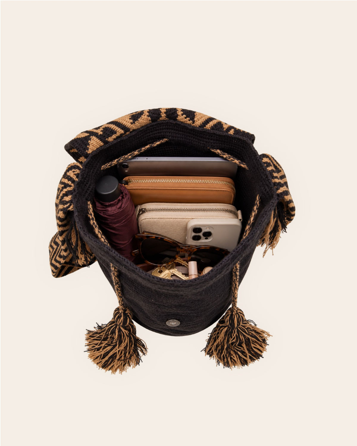 Open black and camel Wayuu crochet Flap Bucket Bag showing its spacious interior with everyday essentials. 
