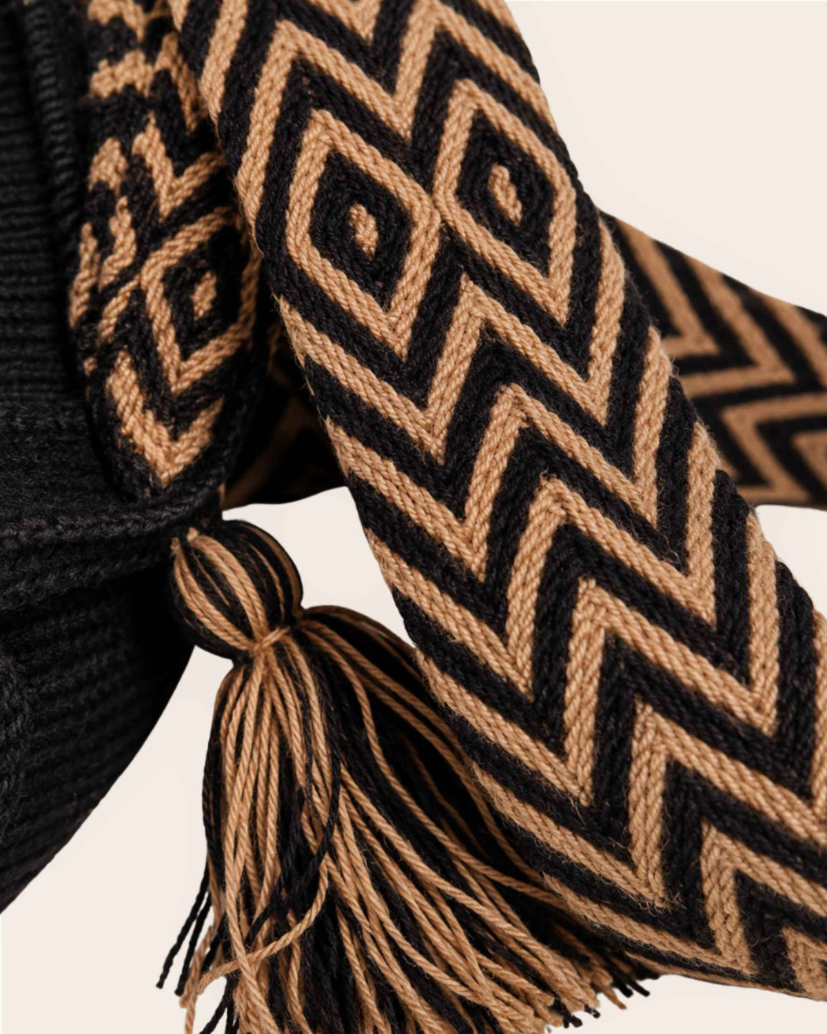 Close-up of the black and camel geometric handwoven shoulder strap and tassel detail of the Wayuu Flap Bucket Bag. 
