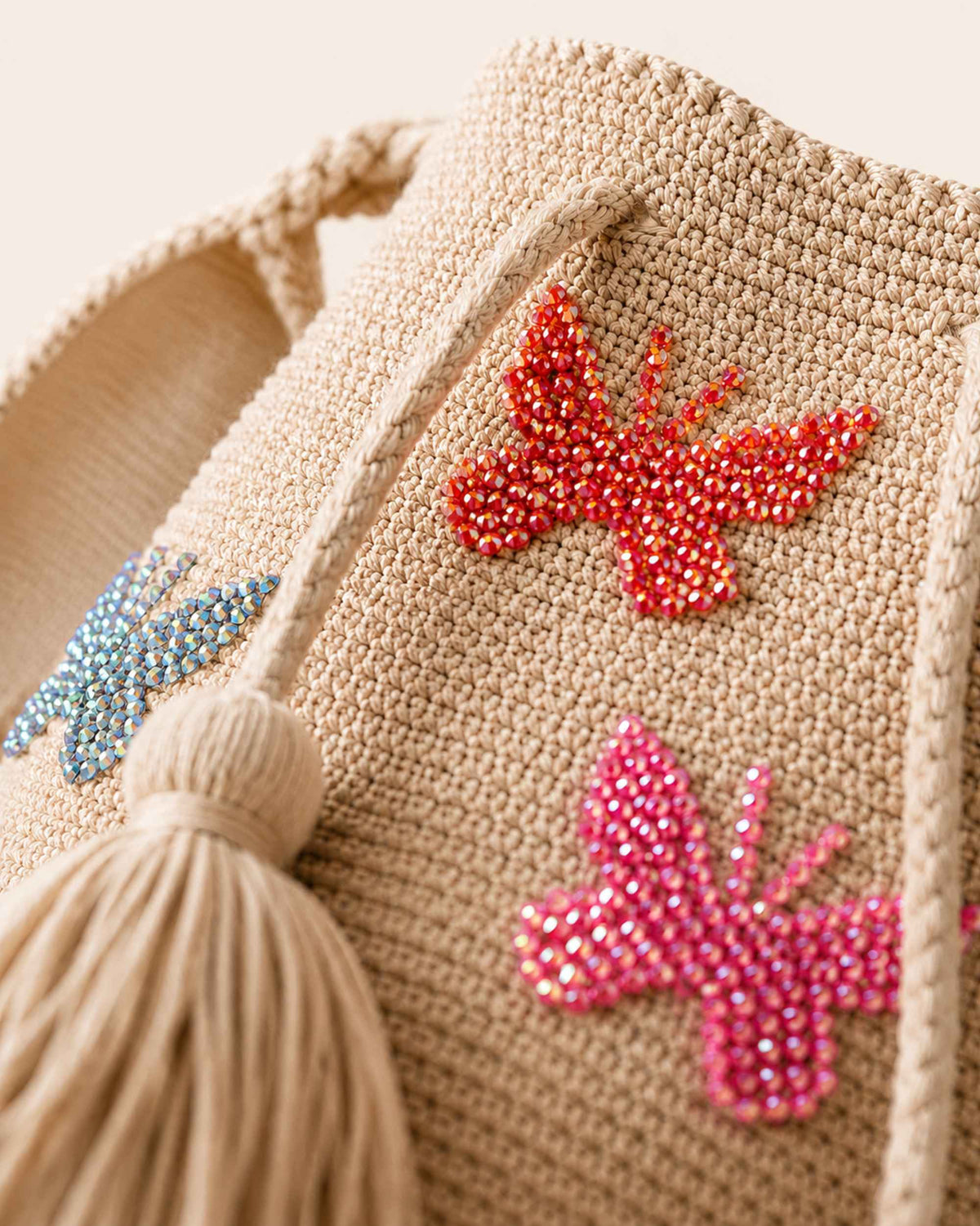 Close-up of red, pink and blue beaded butterfly embellishments and crochet texture on beige Wayuu bag. 