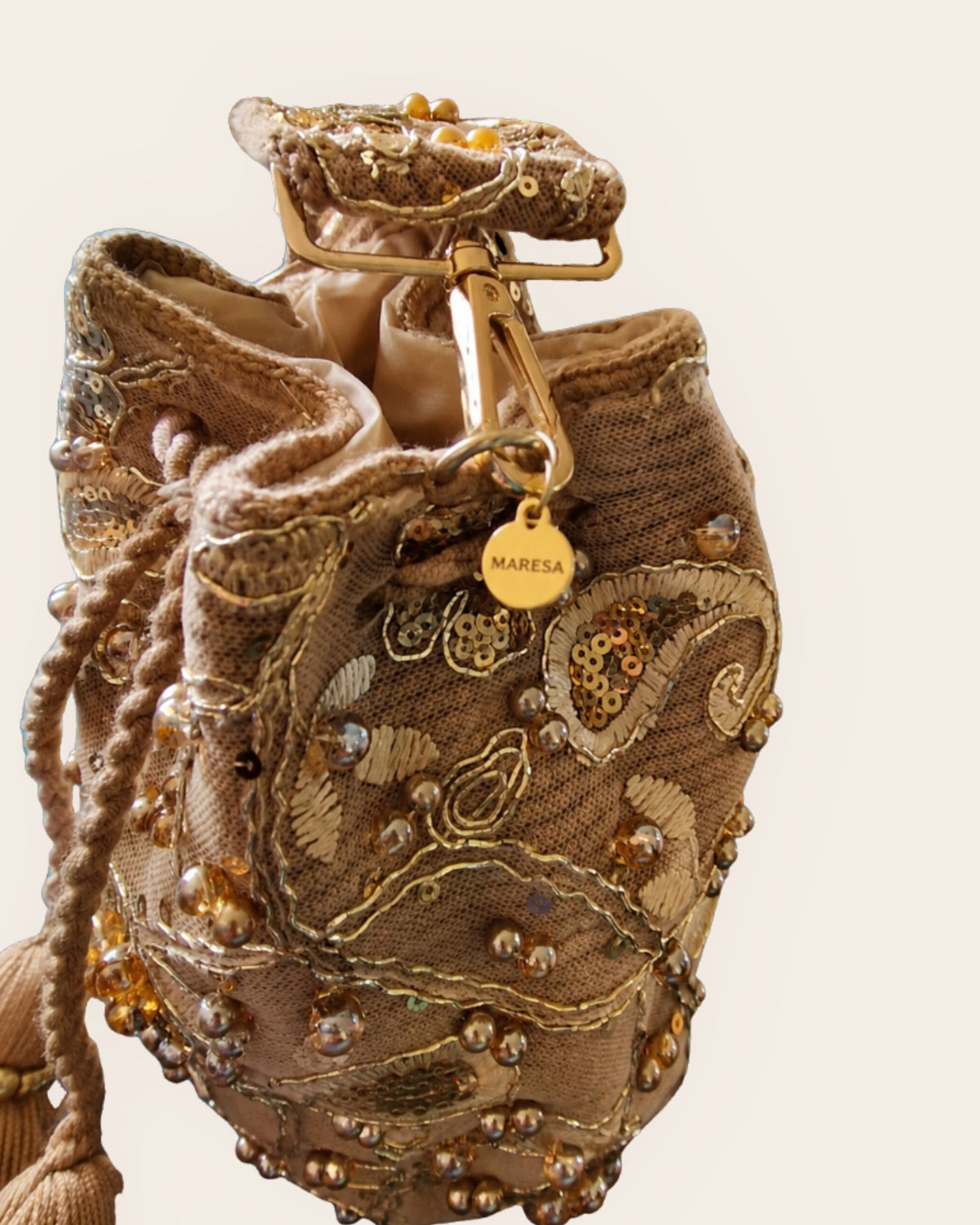 Close-up of gold-tone hardware and Maresa engraved charm on champagne gold embellished occasion bag 