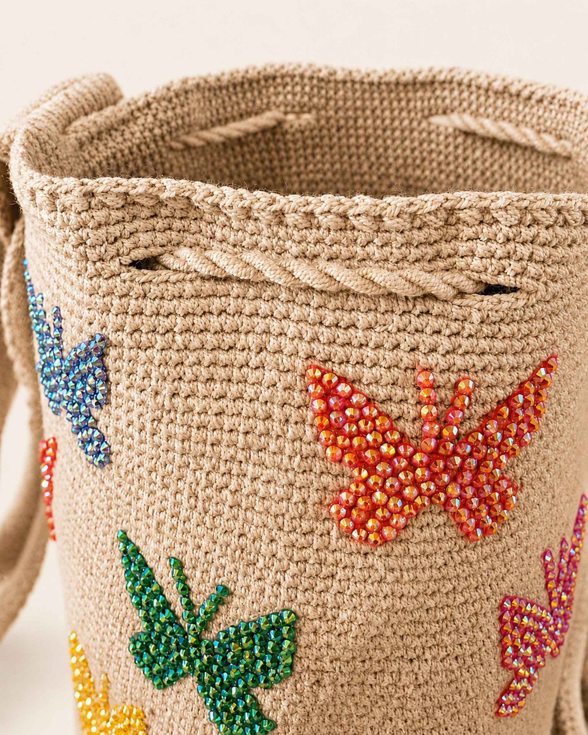 Close-up of beige Wayuu crochet bag with colourful beaded butterflies and handcrafted drawstring closure. 