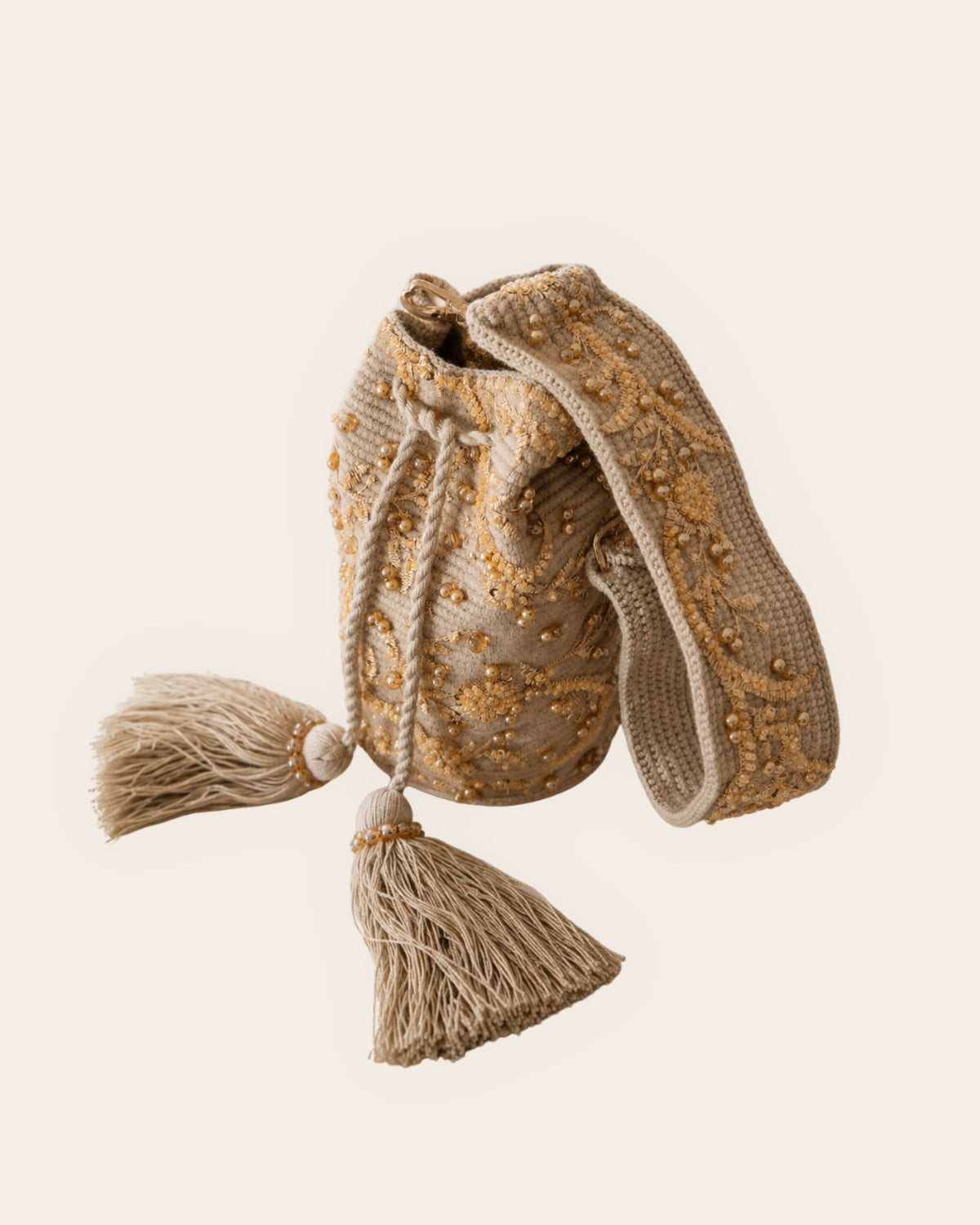 Side view of beige handcrafted occasion bag with embellished handle, gold beadwork, drawstring closure and tassels. 