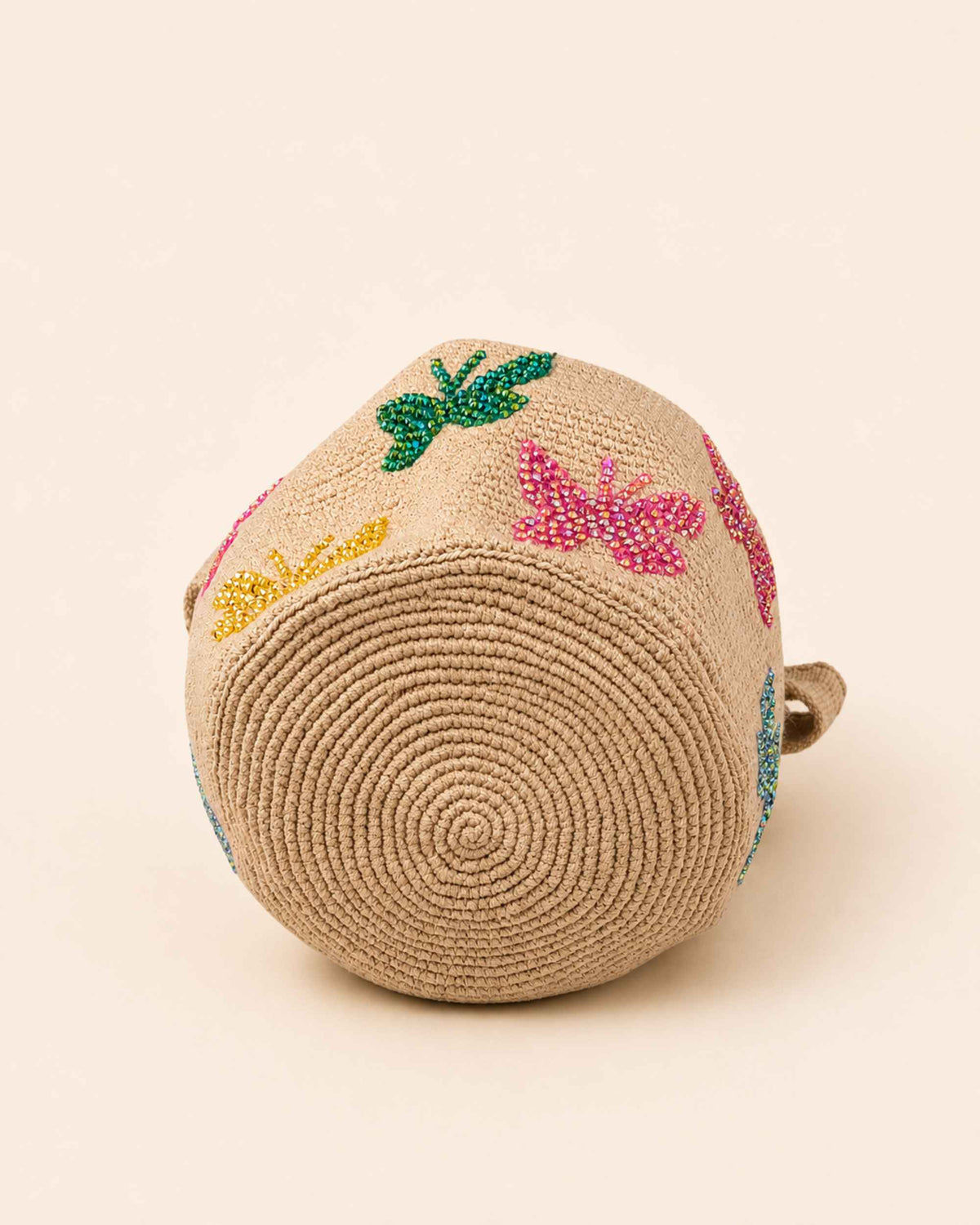 Circular hand-crocheted base of beige Wayuu bag with colourful beaded butterfly embellishments. 